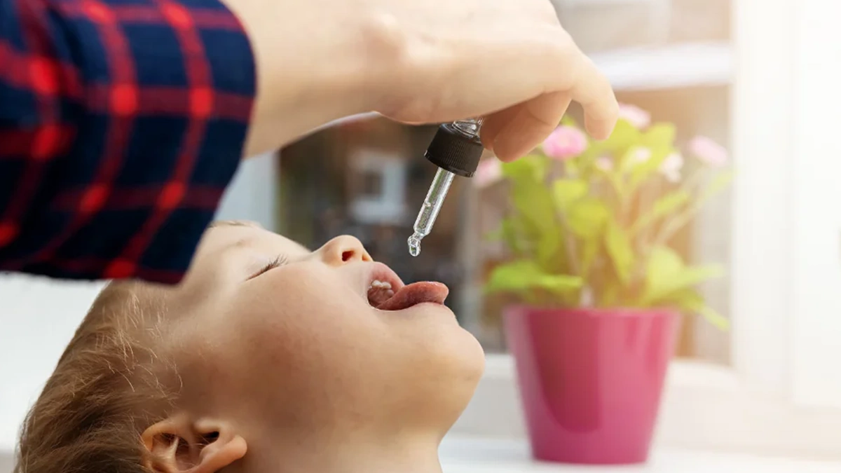 کودکی که دهان خود را باز کرده و فردی با قطره چکان به او مکمل کودکان می دهد