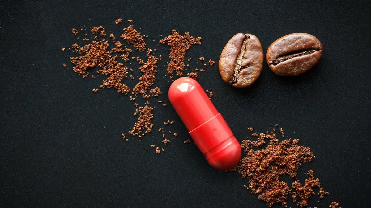 عکس یک کپسول قرمز رنگ در کنار دو دانه قهوه و مقداری قهوه آسیاب شده