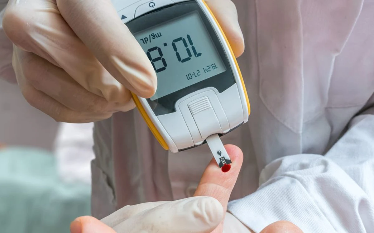 پزشکی که انگشت فرد را گرفته است و با دستگاه تست قند خون از او آزمایش دیابت می گیرد