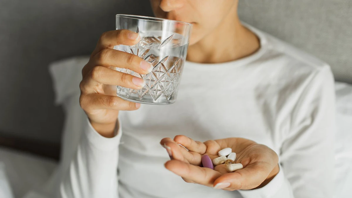 فردی که در یک دست لیوان آب و در دست دیگر چند قرص مولتی ویتامین گرفته است