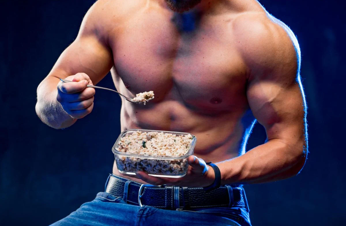 مرد بدنسازی که ظرف حاوی غذای مکمل در دست دارد و یک قاشق پر از غذا در دست راستش گرفته