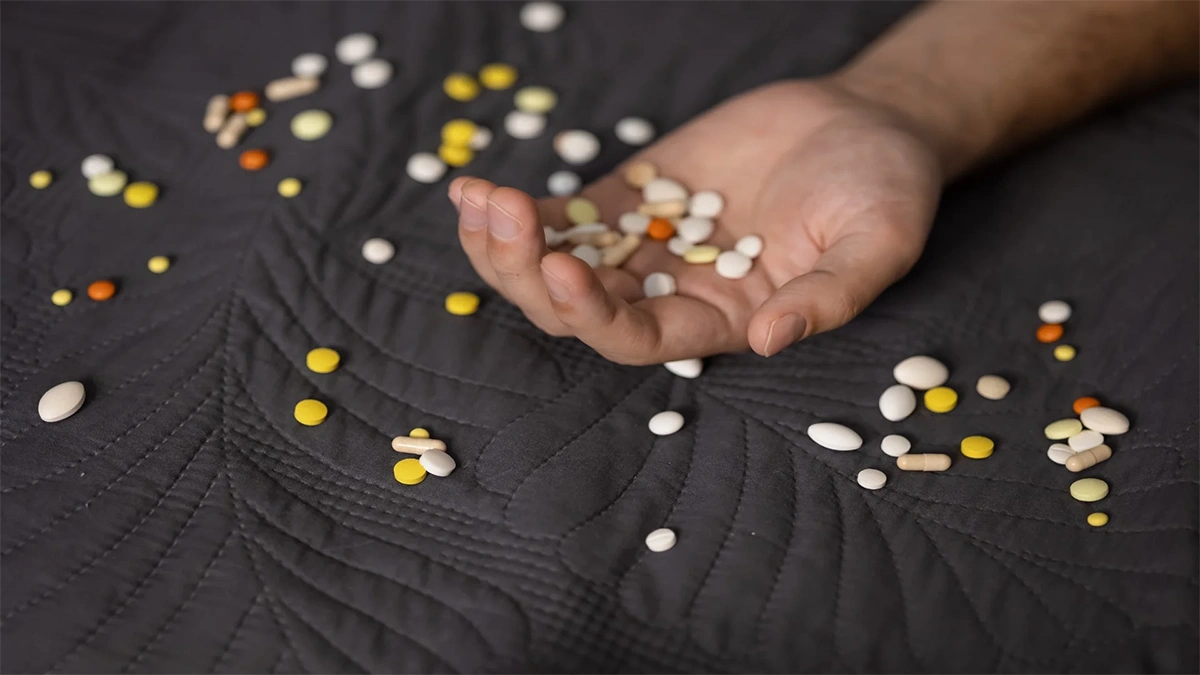 دست فردی که روی یک سطح پارچه ای است و روی دست او تعداد زیادی قرص و کپسول ریخته است