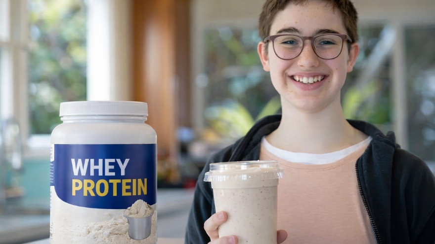 تصویر یک پسر نوجوان که یک لیوان شیک در دست دارد و یک قوطی پروتئین وی در کنار او