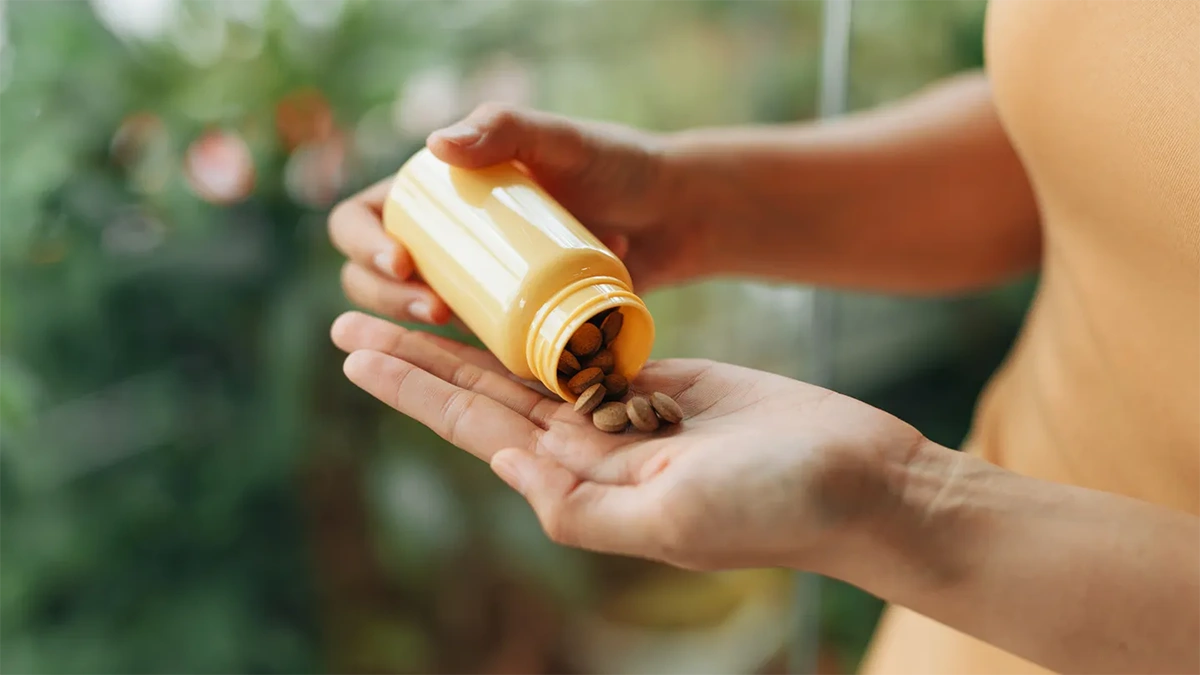 فردی که یک قوطی زرد رنگ مولتی ویتامین در دست دارد و قرص ها را در دست خود خالی می کند