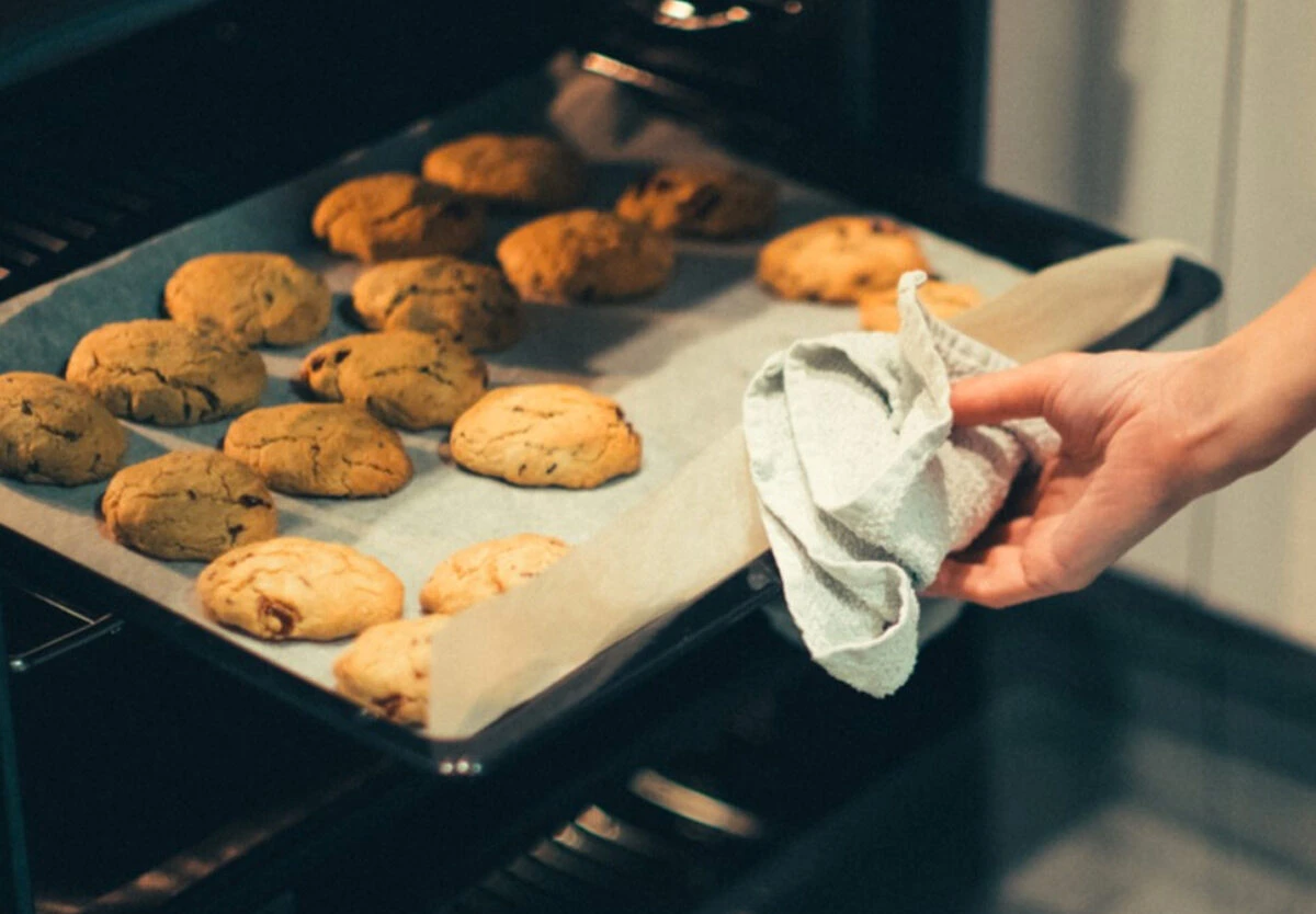 فردی که سینی فر پر از کوکی را از داخل فر بیرون می آورد