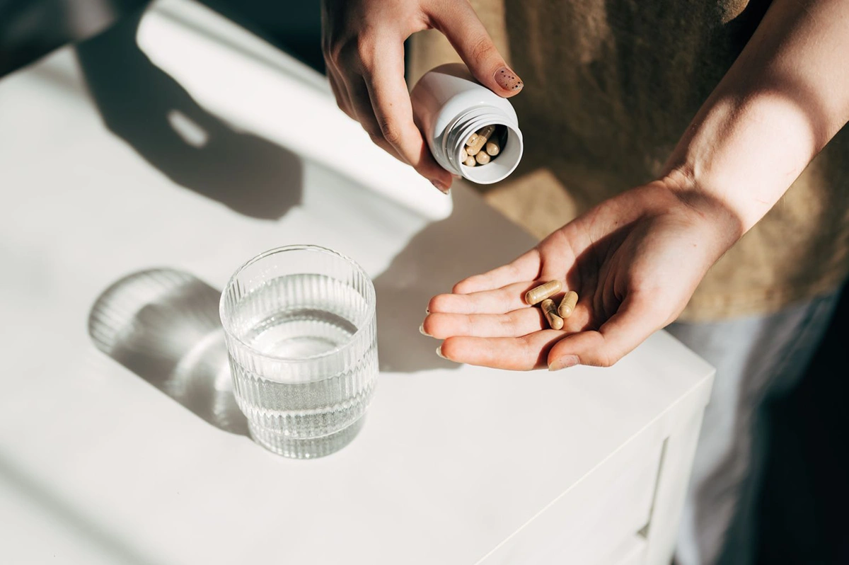 فردی که قوطی قرص را در دست دارد و قرص های مکمل را در دست خود می ریزد